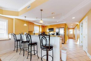 A kitchen with a central island, bar stools, and a trash bin. - Well-Decorated, Ocean Block Condo w/ Fireplace, Balcony & Shared Pool/Gym (Ocean City)