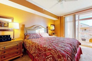 A hotel room with a large bed, a wooden nightstand, a dresser, and a balcony view. - Well-Decorated, Ocean Block Condo w/ Fireplace, Balcony & Shared Pool/Gym (Ocean City)