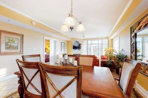 A dining area with a wooden table and chairs, a chandelier, and framed artwork on the walls. - Well-Decorated, Ocean Block Condo w/ Fireplace, Balcony & Shared Pool/Gym (Ocean City)