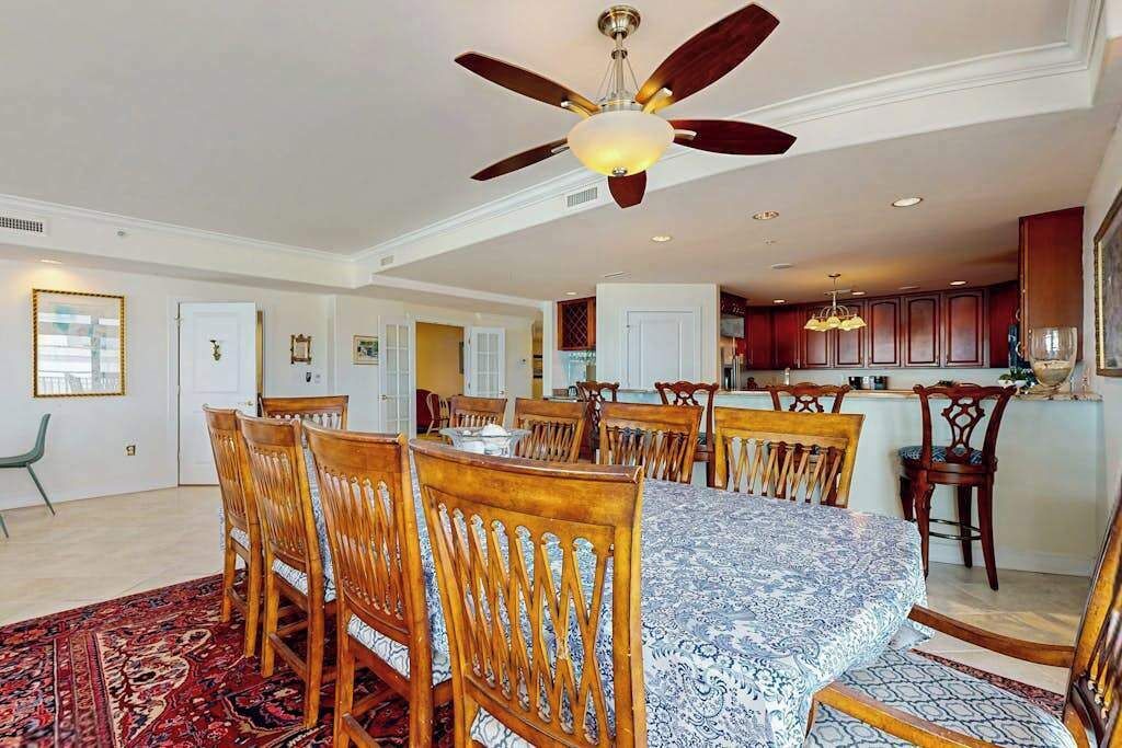 A dining area with a large table, wooden chairs, and a ceiling fan.