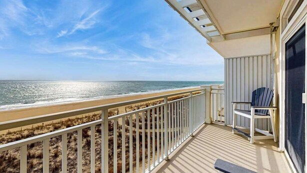 Ein Balkon mit Blick auf Strand und Meer, ein Stuhl und eine Geländer.