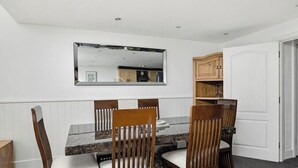 Un coin repas avec une table en marbre, des chaises en bois, un miroir fixé au mur et une cuisine visible dans le reflet.