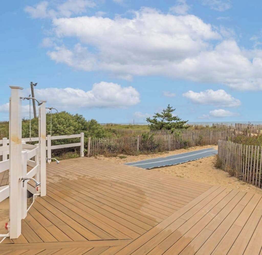 Eine Holzterrasse mit weißem Zaun, einem Weg und einem Strand im Hintergrund.