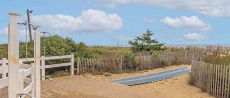 Eine Holzterrasse mit weißem Zaun, einem Weg und einem Strand im Hintergrund.