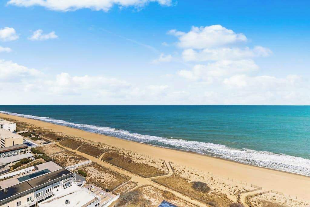 Une propriété située sur la côte, avec vue sur la plage, une zone sablonne agrémentée de sentiers et un bâtiment doté d’un toit plat.
