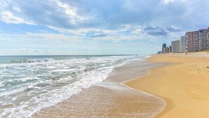 Ein Strand mit sandigem Ufer, Meereswellen und Hochhäusern im Hintergrund.