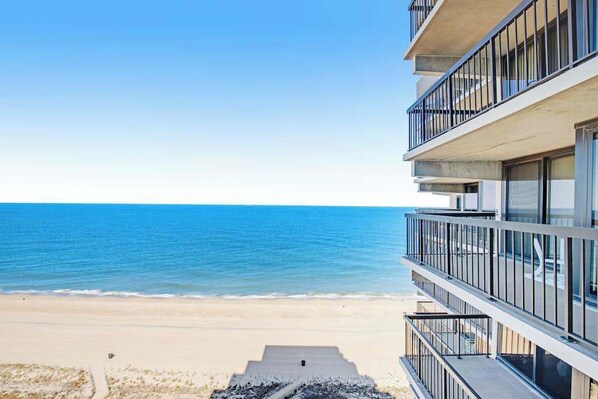 A beachfront hotel with a view of the ocean, balconies, and a concrete pathway leading to the beach. - Sun-kissed beach condo with balcony, pools, game room, tennis & AC (Ocean City)