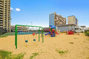 A playground with swings and slides, a small boat structure, and a tennis court. - Beach-view, well-equipped condo with balcony, pools, gym & tennis (Ocean City)