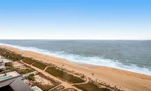 A beach view with a sandy shoreline, a clear sky, and a building with a swimming pool. - Beach-view, well-equipped condo with balcony, pools, gym & tennis (Ocean City)