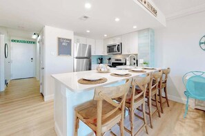 A modern kitchen with white cabinetry, stainless steel appliances, and a central island with bar stools. - Wonderful beachfront condo with balcony, pools, gym, sauna & game room (Ocean City)