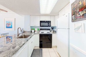 Une cuisine avec des meubles blancs, un micro-ondes noir, une cuisinière et un réfrigérateur.
