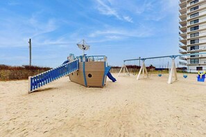 Ein Strandspielplatz mit Rutsche, Schaukeln und einer Holzspielanlage.
