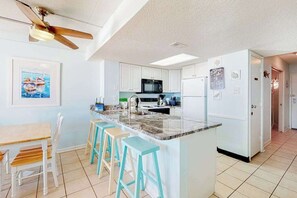 Une cuisine moderne avec des armoires blanches, un comptoir en granit et un ventilateur de plafond.