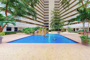 Un hôtel à plusieurs étages doté d’une piscine centrale, entourée de verdure et de palmiers.