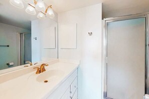 A bathroom with a white sink, a mirror, and a shower. - Stunning beach condo with balcony, views, pools, gym, game room & sauna (Ocean City)