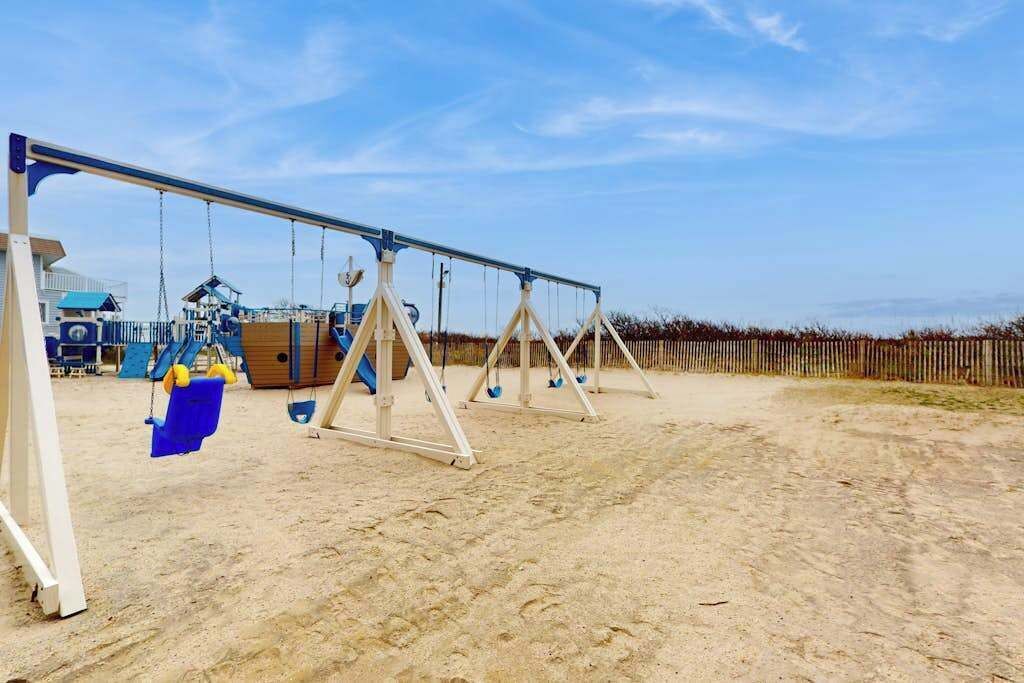 A sandy outdoor area with swings and a wooden fence.
