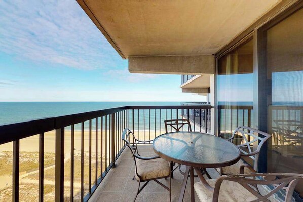 A balcony with a table and chairs overlooking a beach. - Modern beach condo with balcony, pools, gym, game room & sauna (Ocean City)