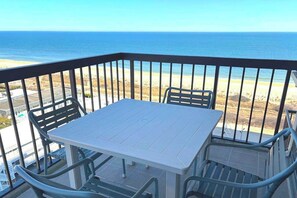 Ein Balkon mit Tisch und Stühlen mit Blick auf einen Strand und den Ozean.