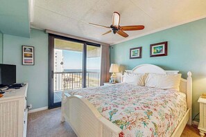 Ein Schlafzimmer mit einem Bett, einem Deckenventilator, einem Schreibtisch mit Fernseher und einem Balkon mit Blick.