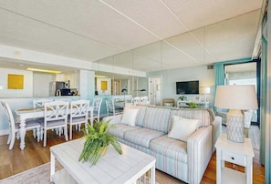 Ein modernes Wohnzimmer mit Sofa, Esstisch, Stühlen und einem durch eine Glaswand sichtbaren Küchenbereich.