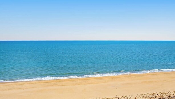 A beach with clear blue water and a sandy shore. - Sunny beach condo with balcony, game room, pools, sauna & gym (Ocean City)