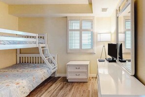 A bedroom with a bunk bed, a bedside table, a desk with a computer, and a window with blinds. - Remodeled, ocean-view condo with pools, saunas & gym (Ocean City)