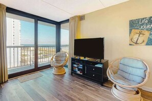 Ein Wohnzimmer mit einem großen Fenster, einem Fernseher und zwei Korbsesseln.