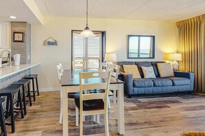 Ein Wohnzimmer mit Essbereich, einer Couch, einem Kronleuchter und einem Fenster mit Vorhängen.