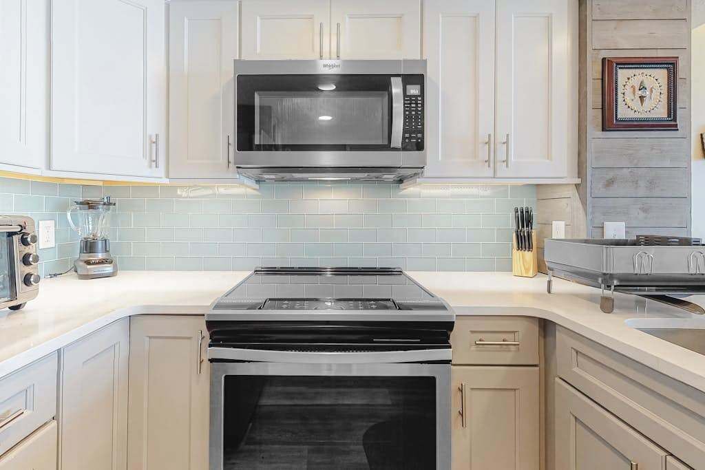 A kitchen with white cabinets, a microwave, a stove, and a sink.