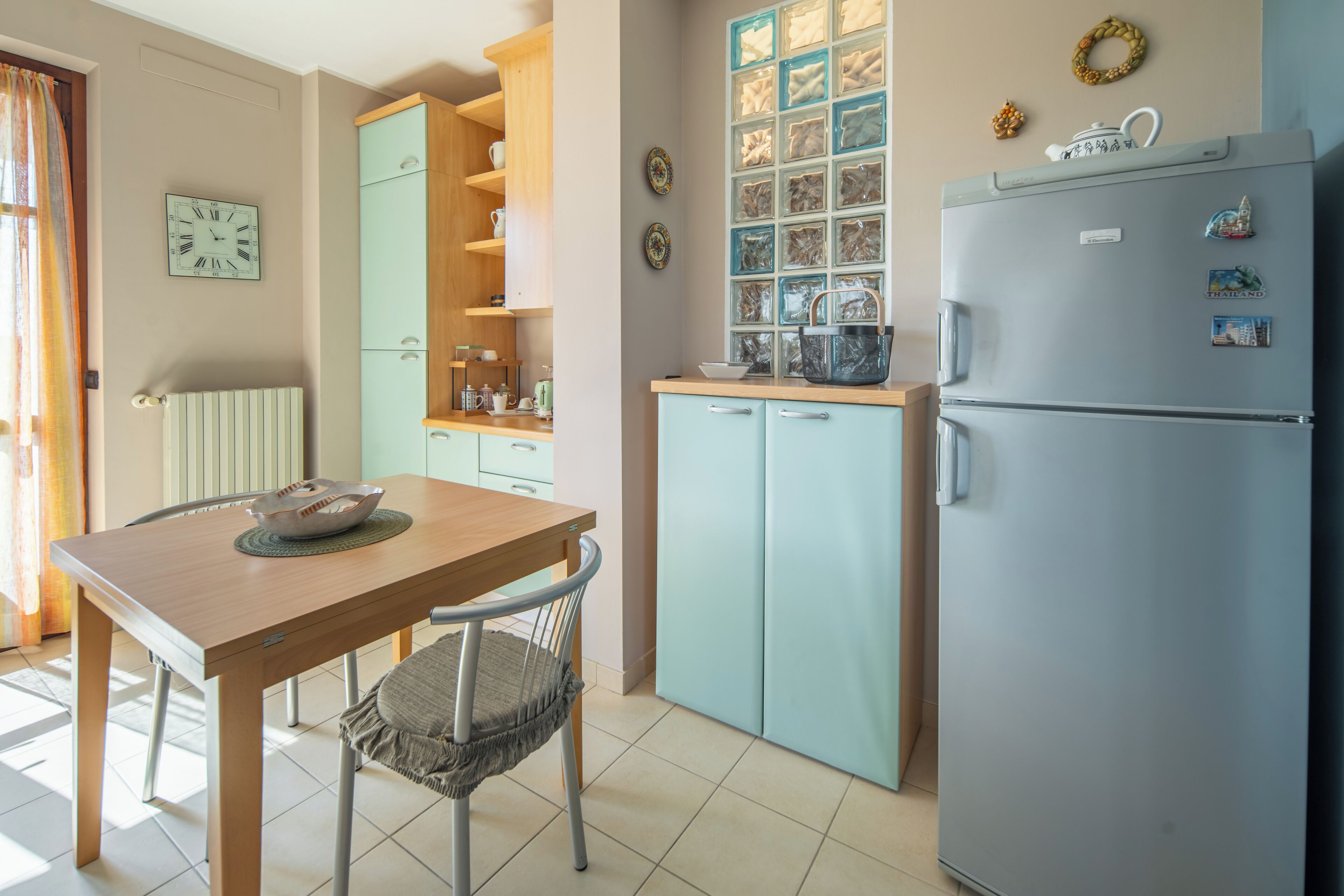 A kitchen with a wooden table, a chair, a refrigerator, and a window with blinds.