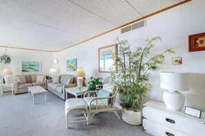 A living room with a sofa, chairs, a coffee table, a lamp, a potted plant, and artwork on the walls. - Oceanfront condo with two balconies, bay & ocean views, AC, WiFi, shared pool (Ocean City)