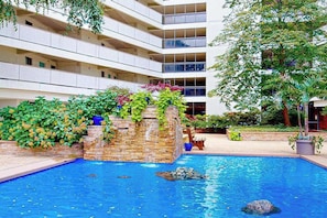 Ein Hotel mit Pool, einem Wasserfall aus Stein und einem mehrstöckigen Gebäude mit Balkonen.