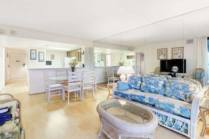 A living room with a sofa, chairs, a glass coffee table, and a television. - Sunny, inviting condo near the beach with balcony, pools & gym (Ocean City)