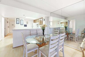 A modern kitchen with white cabinets, a glass dining table, and a central island. - Sunny, inviting condo near the beach with balcony, pools & gym (Ocean City)
