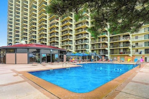 A swimming pool with a covered area, surrounded by multi-story residential buildings. - Sunny, inviting condo near the beach with balcony, pools & gym (Ocean City)