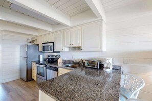 A kitchen with white cabinets, a granite countertop, stainless steel appliances, and a white chair. - Oceanfront Townhouse w/Private Balcony, Great Views, Washer/Dryer, Central AC (Ocean City)