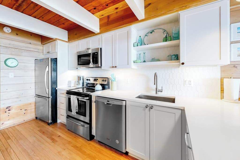 A modern kitchen with white cabinets, stainless steel appliances, and a wooden ceiling.