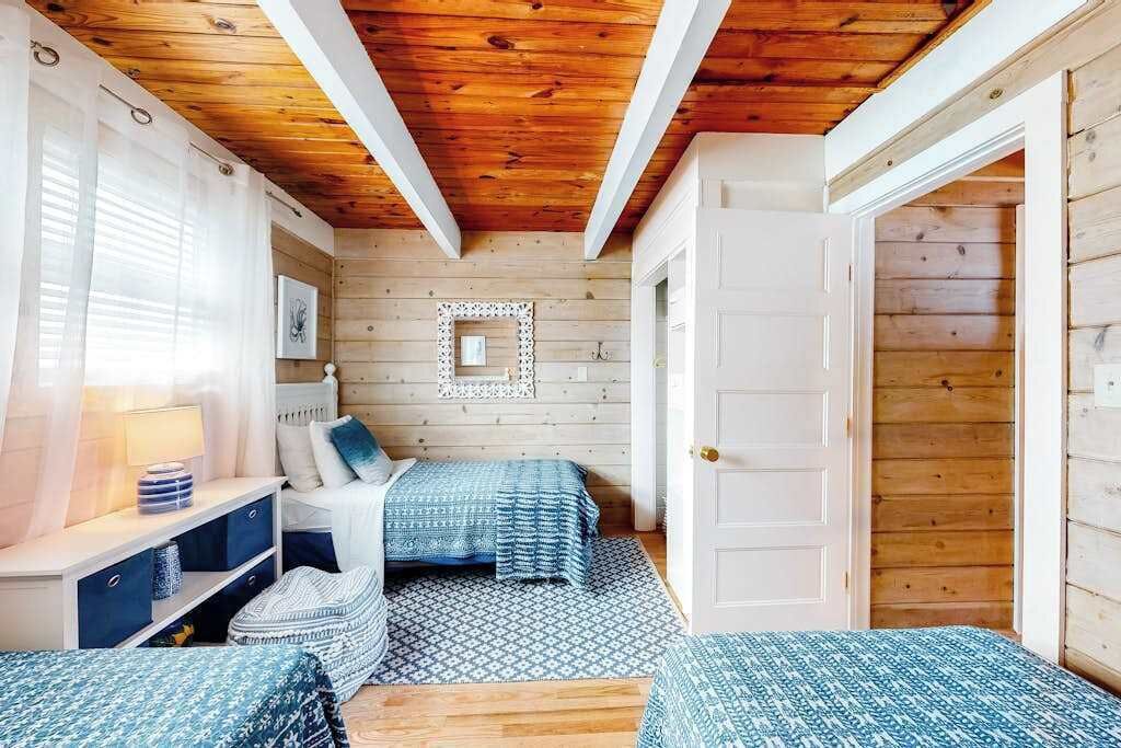 A cozy bedroom with a wooden ceiling, two beds with patterned bedding, a bedside table, and a nightstand.