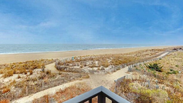 Une vue sur la plage avec une clôture en bois, une plage de sable et l’océan.