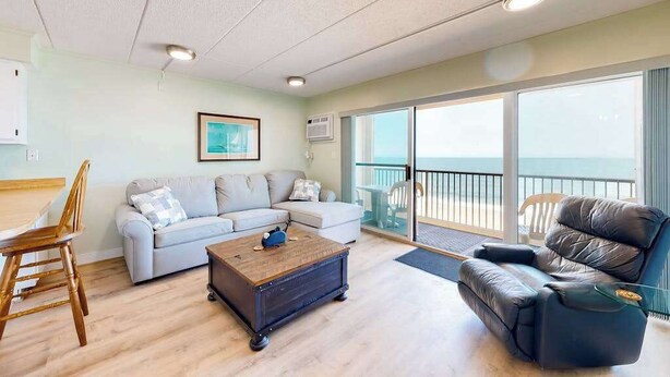 Een woonkamer met een bank, een fauteuil, een salontafel en uitzicht op de oceaan door grote ramen.