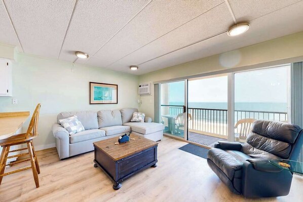 A living room with a sofa, a recliner, a coffee table, and a view of the ocean through large windows. - Sandpiper Dunes 808 (Ocean City)