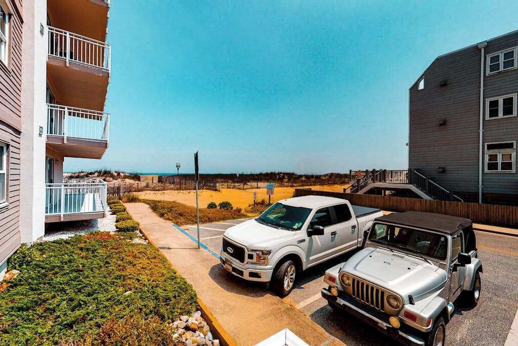 Un espace de stationnement avec deux VUS, un immeuble doté de balcons et une vue sur la plage.