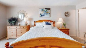 Quarto com cama de madeira, duas mesas de cabeceira com luminárias, cômoda, espelho e uma obra de arte pendurada na parede.