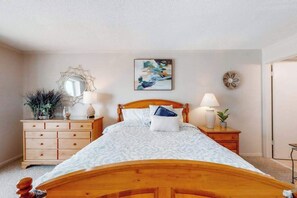 A bedroom with a wooden bed, two bedside tables with lamps, a dresser, a mirror, and a wall-mounted artwork. - Inviting Beach Condo w/Private Balcony, Great Location, Washer/Dryer, Central AC (Ocean City)