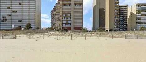 A beachfront hotel with multiple high-rise buildings, sandy beach in front, and a clear sky.