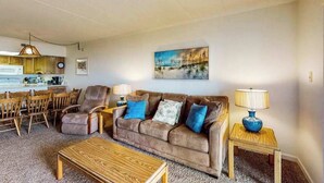 A living room with a brown sofa, two blue cushions, a wooden coffee table, and a lamp on a side table.