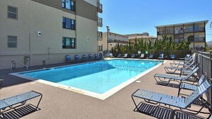 A swimming pool with lounge chairs and a building with multiple floors and balconies.