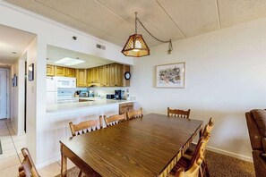 Ein Essbereich mit Holztisch und -stühlen, eine Küche mit Holzausstattung, einer Pendelleuchte und einem gerahmten Bild an der Wand.