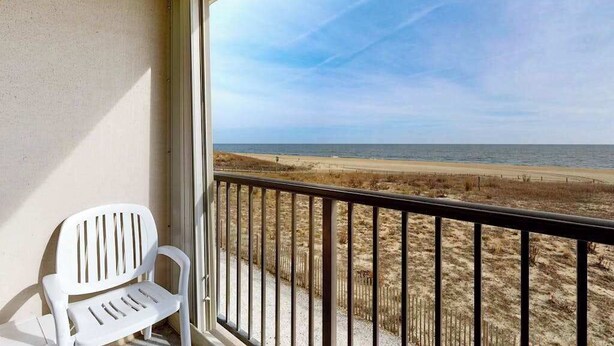 A balcony with a white chair, a view of the beach, and a clear sky.