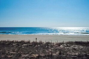 A beach with a clear sky, sandy shore, and sparse vegetation. - Sandpiper Dunes 204 (Ocean City)
